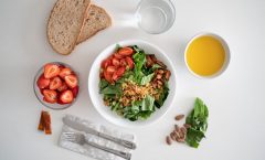 Top view of a healthy salad and fresh ingredients with bread and juice on a white surface.